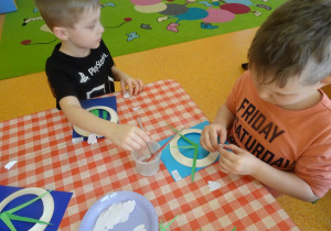 Dwóch chłopców nakleja białe pąki kwiatów na kartę papieru.